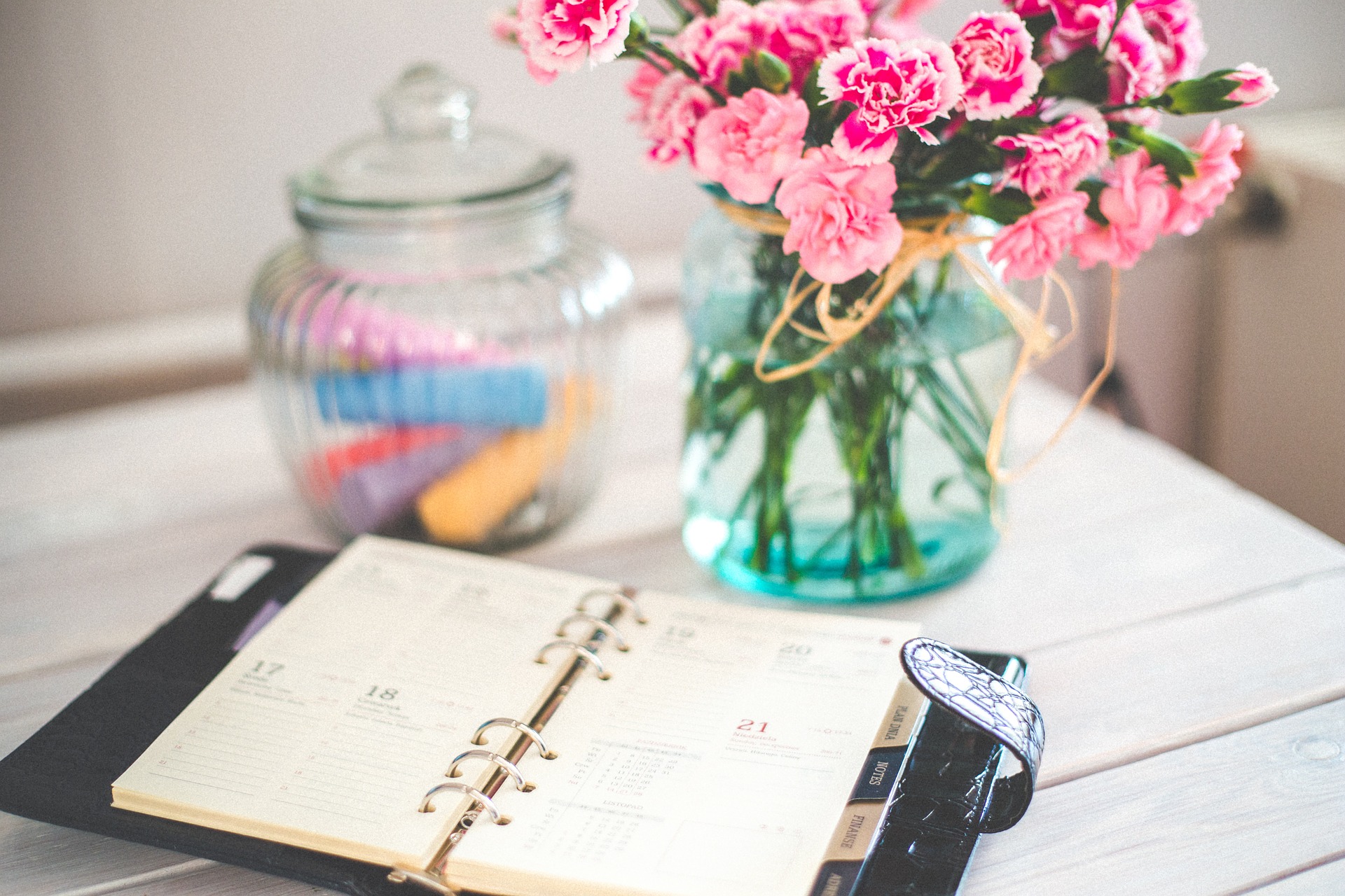 Appointment book open on a desk by some pink flowers